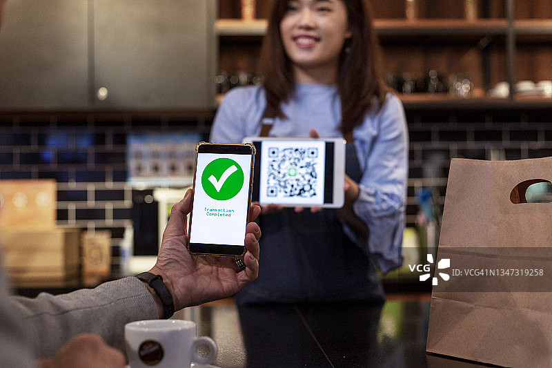 咖啡馆店主使用智能手机接收顾客的移动支付图片素材