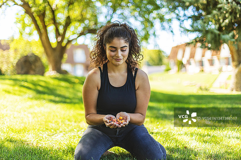 拉丁裔少女在自家前院放松，手拿并抛掷海棠果图片素材