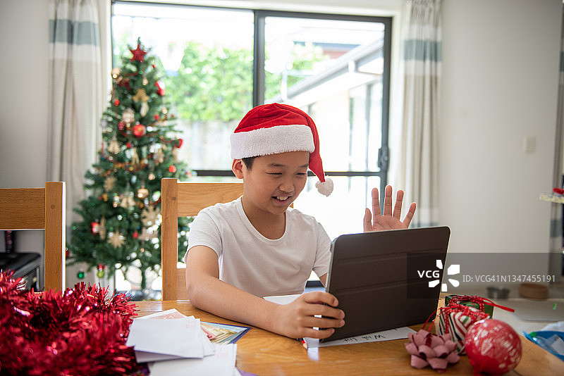 在客厅圣诞树前的桌子上使用ipad的青少年男孩图片素材