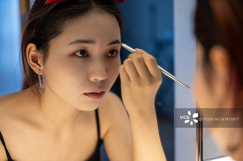 穿着吊带裙的美丽女人在镜子前化妆图片素材