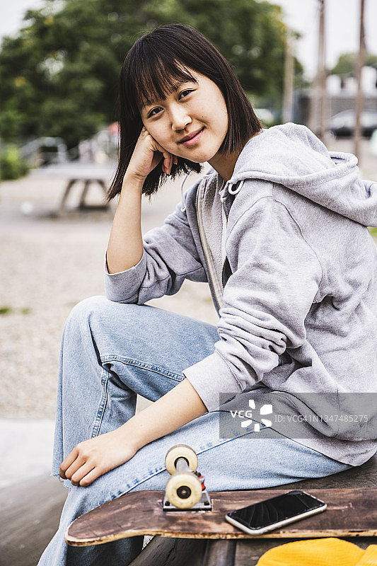 微笑的少女坐在长椅上，手持智能手机和滑板图片素材