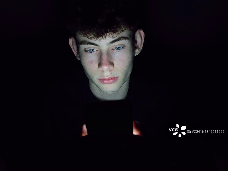 在黑暗中阅读手机的年轻少年肖像图片素材