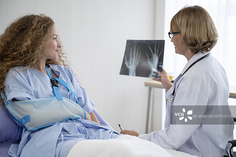 在医院，医生们正在翻译一位手臂骨折的妇女的X光片，她的手臂折叠起来缠绕在手上。图片素材