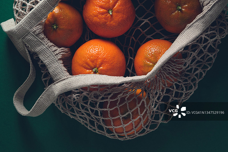 绿色背景下，再生材料环保袋中的未成熟橘子。素食、纯素食和生食。环保、回收概念。有机农场环保产品图片素材