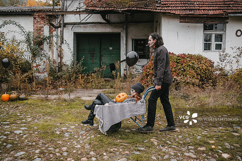 万圣节概念：坐在建筑手推车里的女人被一个可怕的男人推着图片素材