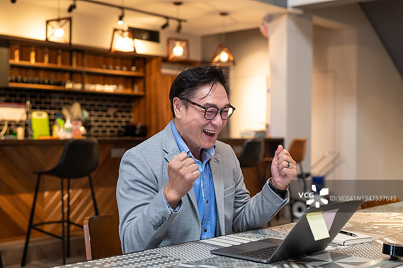 在办公室使用笔记本电脑，收到股市投资喜讯而兴奋的亚洲商人图片素材
