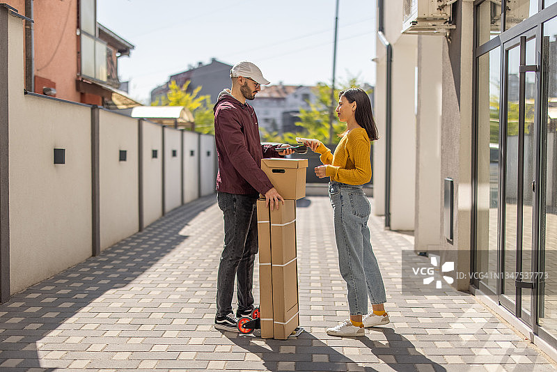 年轻微笑的女人在人行道上用手机向送货员进行非接触式支付图片素材