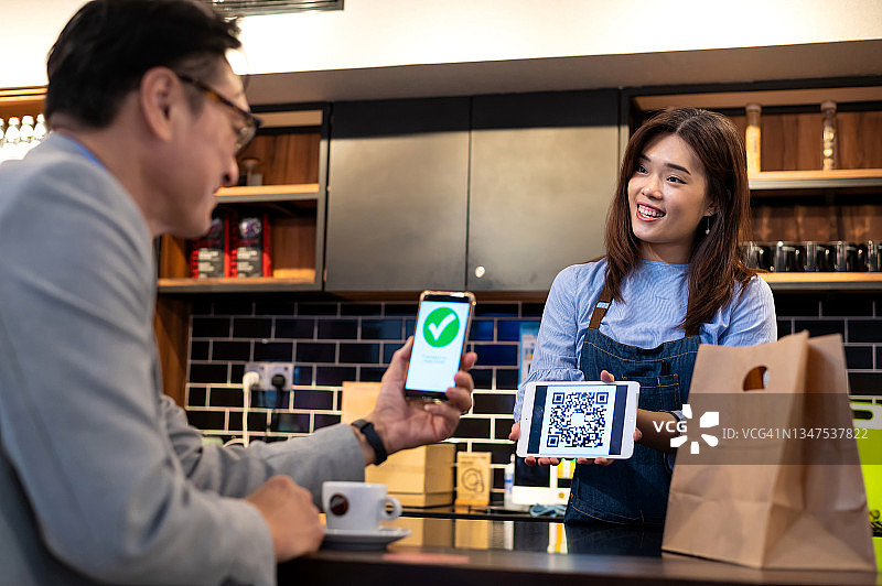 年轻的亚洲女服务员在咖啡馆使用智能手机接收顾客的无线支付图片素材
