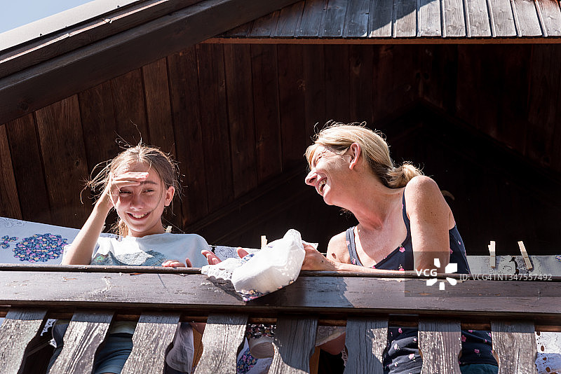 微笑的母亲和女儿在夏日里在小屋阳台上晾晒洗好的窗帘图片素材