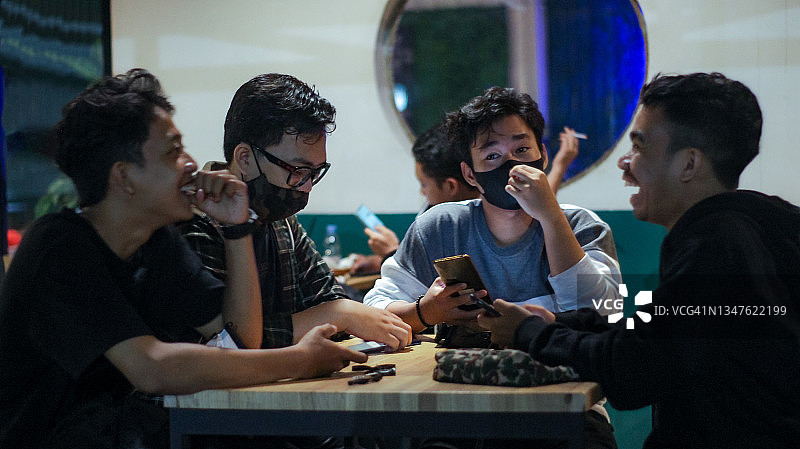 一群年轻人在夜晚的咖啡馆里聊天和使用手机图片素材