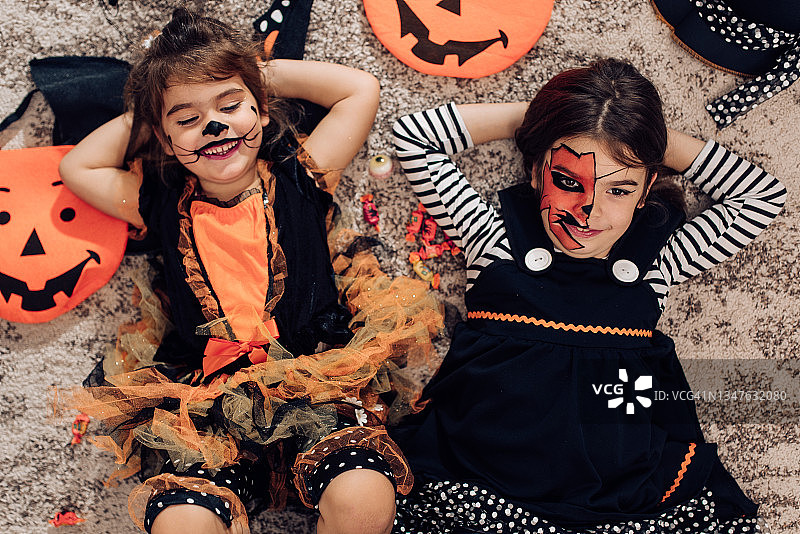 两个装扮成万圣节的可爱小姐妹躺在地板上图片素材
