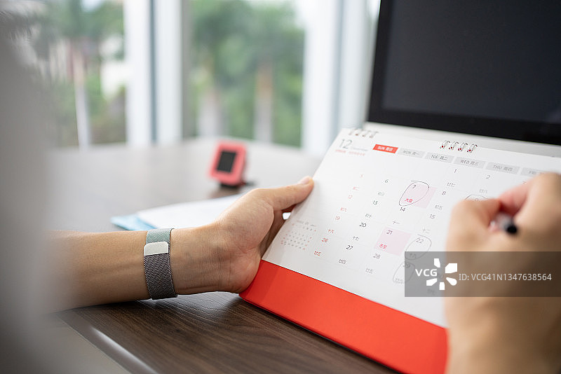 亚洲商人在办公桌日历上做标记图片素材