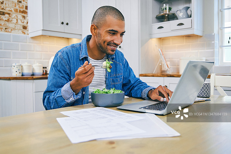 年轻男人在家使用笔记本电脑和健康沙拉的照片图片素材