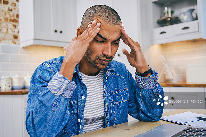 在家工作时，使用笔记本电脑的年轻男子看起来压力很大图片素材