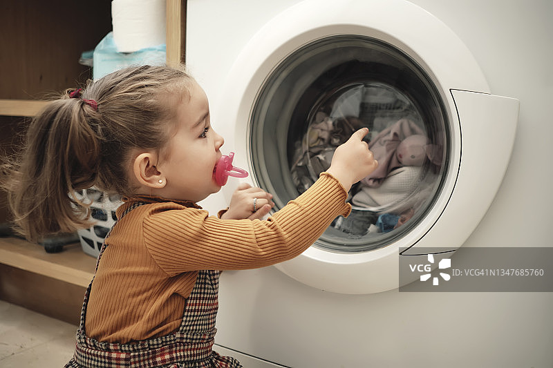 女孩看着她睡觉的娃娃在洗衣机里洗涤图片素材