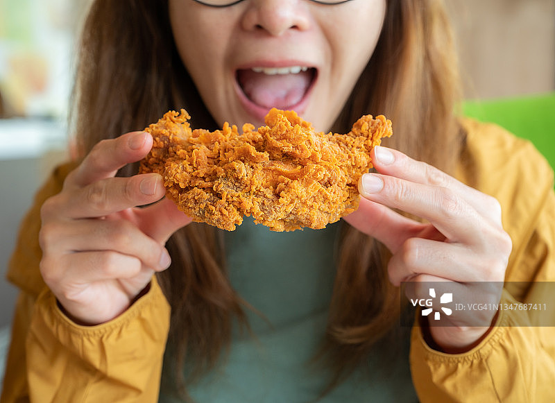 年轻的亚洲女性张开嘴，准备吃一块香脆的炸鸡图片素材