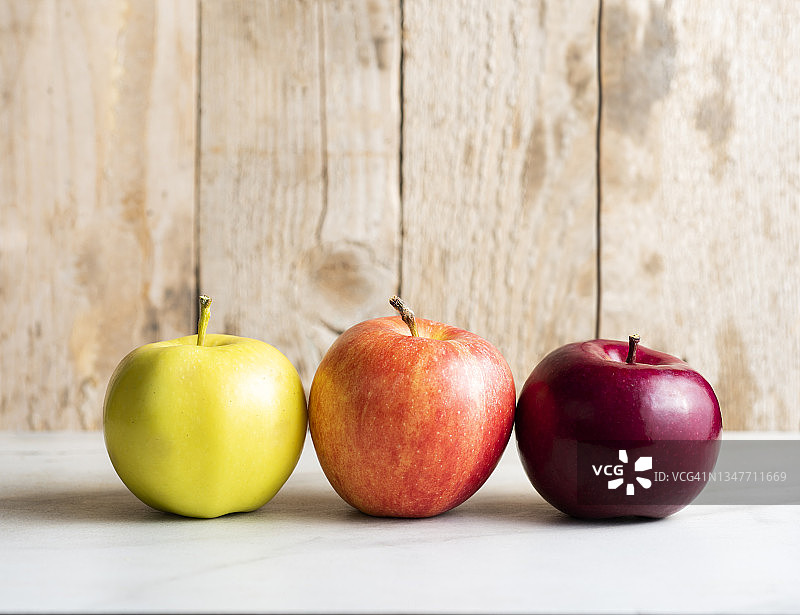 不同种类的苹果在浅色表面和乡村木质背景上的侧视图图片素材