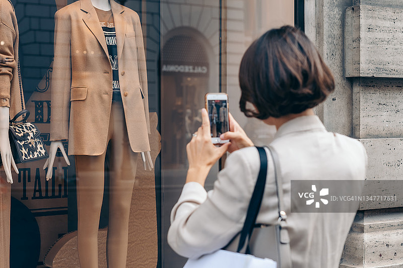 年轻女人在罗马用智能手机拍摄Max Mara精品店的橱窗，意大利购物促销图片素材