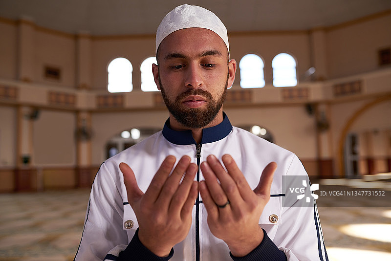 年轻穆斯林男子在清真寺祈祷时举起双手的场景图片素材