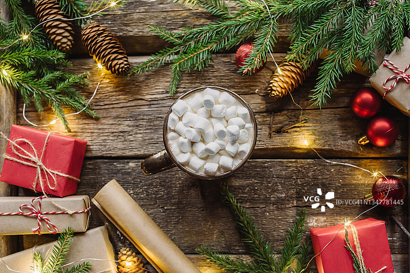 圣诞节或新年组合，包括礼品盒、冷杉树枝、红球、闪光灯、纸卷和一杯可可，上面有木制背景上的棉花糖。平放，俯视图。圣诞快乐卡片图片素材