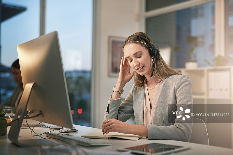 年轻女子在现代办公室里戴着耳机，看起来压力很大图片素材