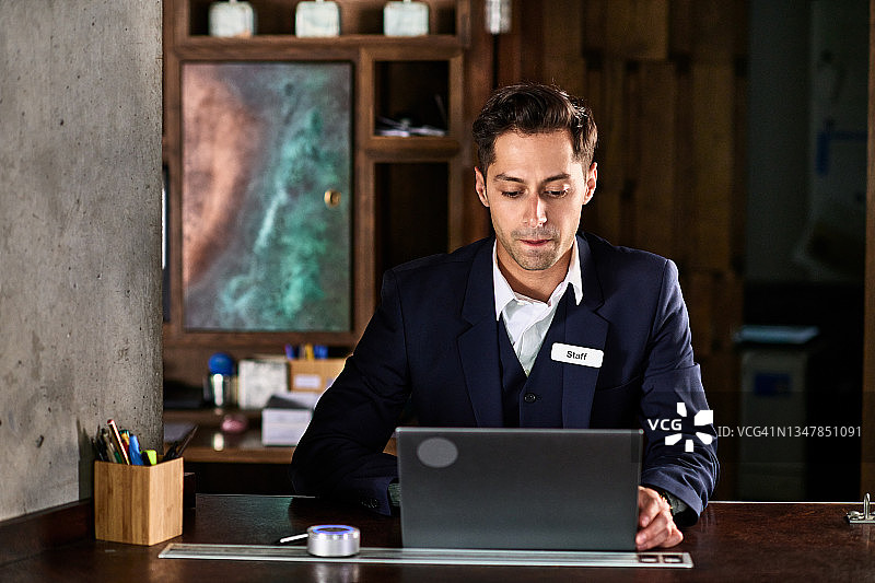 在办公桌前看笔记本电脑的酒店男接待员图片素材