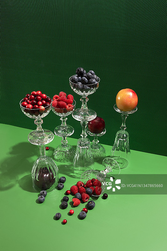 蔓越莓、蓝莓、覆盆子、李子和香槟酒杯在绿色背景中图片素材