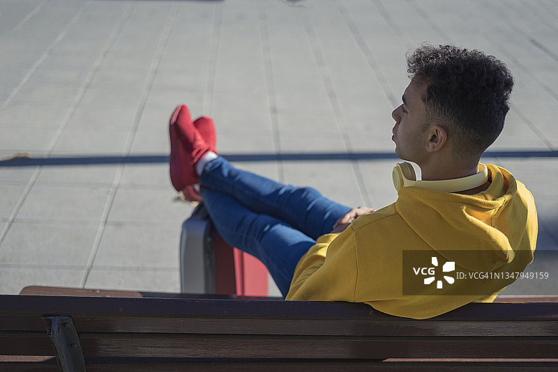 混血男孩坐长凳脚踩行李箱图片素材