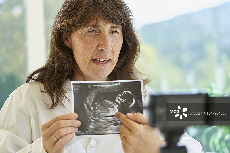 医生拿着超声波照片，前面有一个摄像头，医生在录制视频时解释关于婴儿超声波的情况图片素材