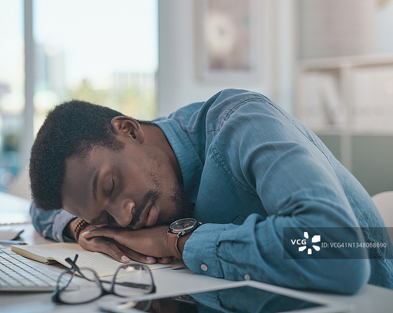 年轻商人趴在现代办公室的桌子上睡觉图片素材