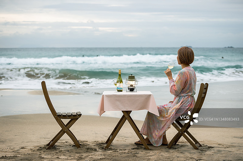 傍晚，情侣在美丽的海滩上欣赏海景，品尝葡萄酒图片素材