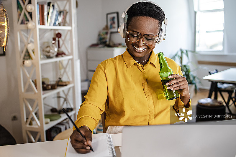 年轻女人放松地坐在海滩上喝啤酒，使用笔记本电脑工作图片素材