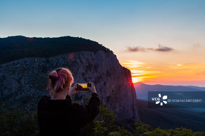 女孩用手机拍摄山顶日出美景图片素材