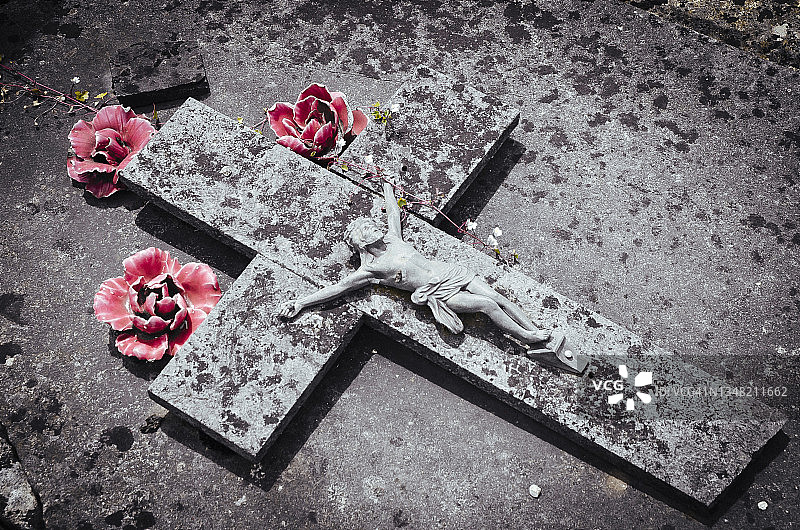 十字架上的耶稣，在装饰着粉红色花朵的灰色旧墓碑上图片素材