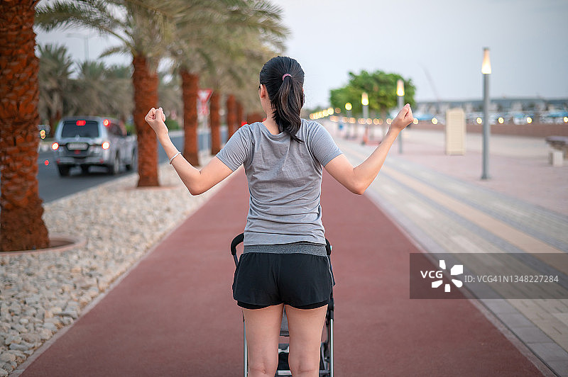 在跑道上做伸展运动，同时用婴儿车推着新生儿的健壮亚洲女性图片素材