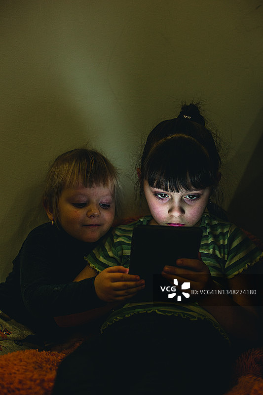夜晚：两个小女孩在黑暗的房间里使用平板电脑图片素材