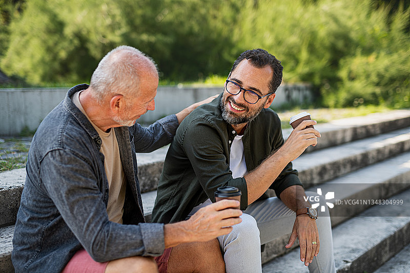 老年男人和中年儿子坐在公园里户外喝咖啡图片素材