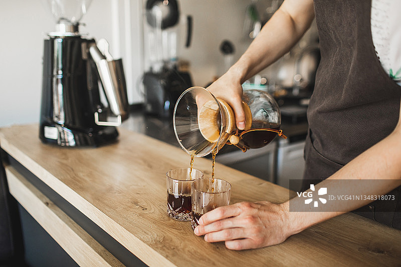 男人将新鲜冲泡的过滤咖啡倒入玻璃杯中。咖啡师职业图片素材