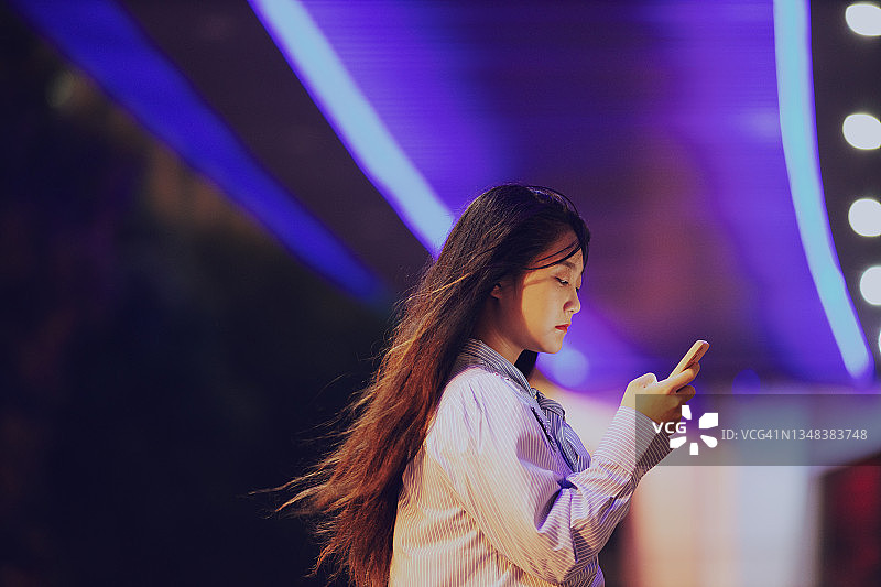 年轻亚洲女人在夜晚天桥下使用手机图片素材