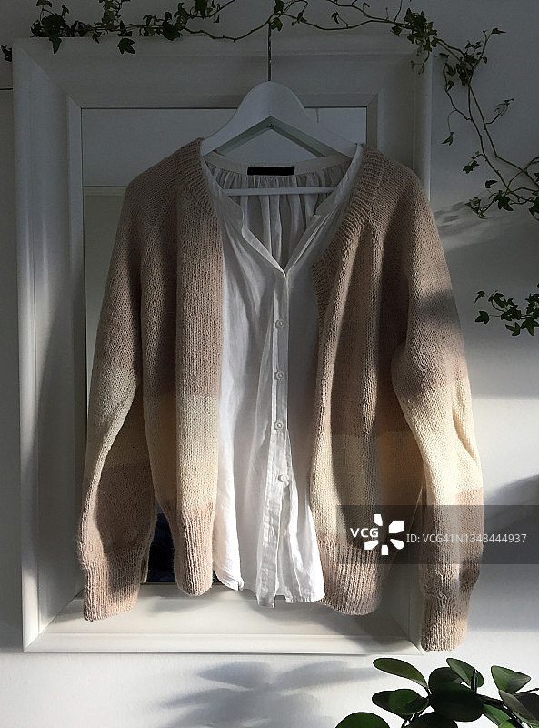 粉色针织毛衣，搭配白色衬衫，挂在镜子前的衣架上图片素材