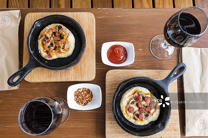 意大利美食：美味的自制披萨，配有培根和黑橄榄，红酒杯，在铁锅中供应图片素材