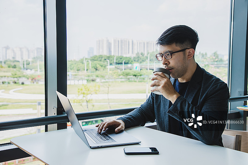 亚洲商人一边喝咖啡一边看笔记本电脑图片素材