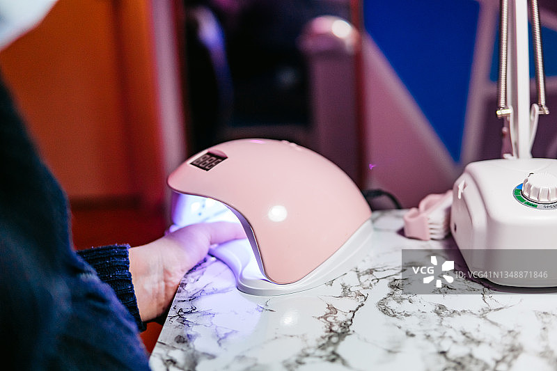 在美容院将拇指放入UV灯美甲烘干机的女顾客图片素材