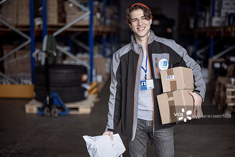 微笑的快递员在仓库手拿包裹看向镜头图片素材