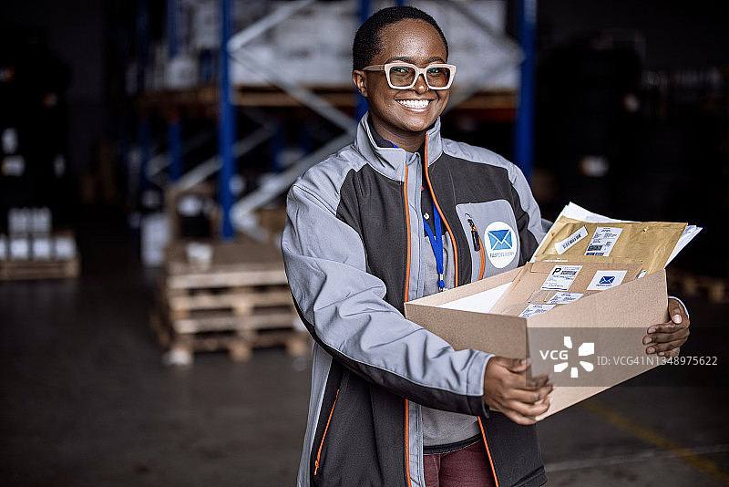 面带微笑的女快递员在仓库中看向镜头图片素材