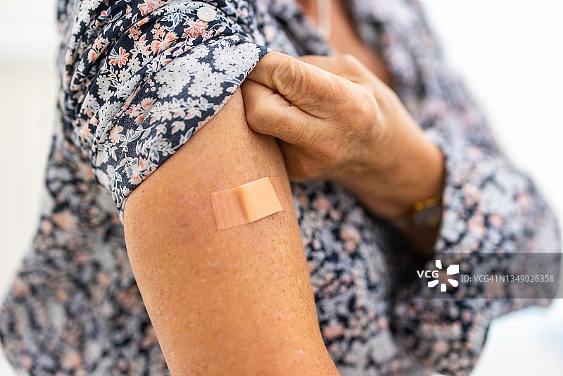 接种新冠疫苗后，女人展示手臂和创可贴图片素材
