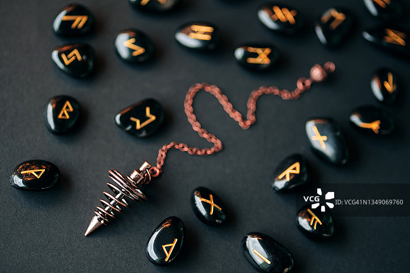 黑色背景下，青铜探测摆锤和黑曜石制成的金色文字符文。魔法神秘仪式概念，扁平风格的宏观摄影图片素材