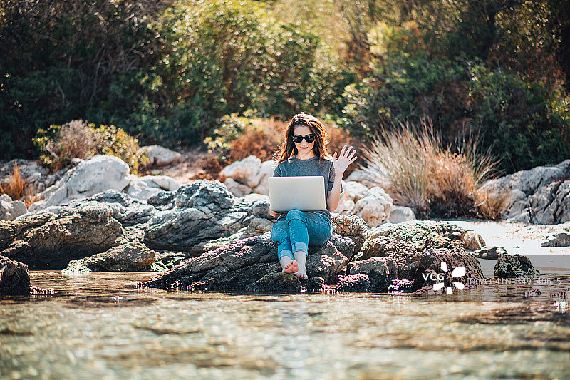 年轻女子在海滩上用笔记本电脑进行视频通话图片素材