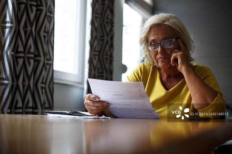 正在阅读报告的金发年长女士，神情专注而担忧。图片素材