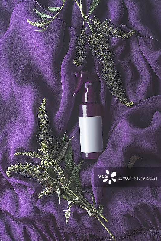 带有紫色纺织背景和绿色丁香枝的化妆品，带有空白标签模型图片素材